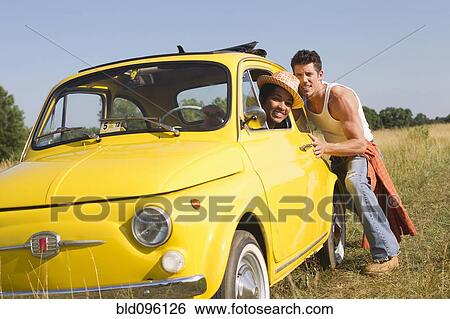 Stock Photograph - Man pushing girlfriend in broken down car. Fotosearch