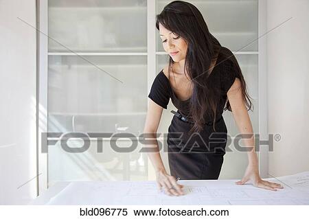 Stock Photography - Mixed race businesswoman looking at blueprints in office. Fotosearch