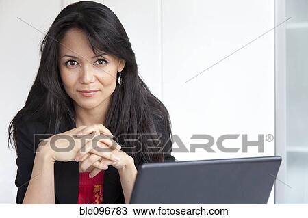 Stock Image - Mixed race businesswoman sitting with laptop. Fotosearch