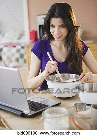 Stock Image - Mixed race woman baking and using laptop. Fotosearch
