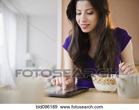 Stock Photo - Mixed race woman eating breakfast and using digital tablet. Fotosearch