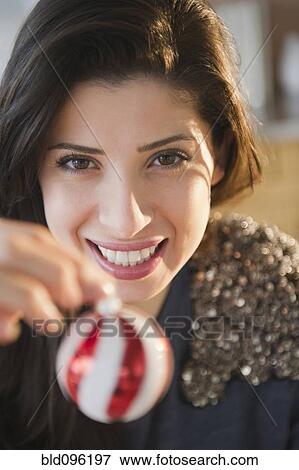 Stock Photo - Mixed race woman holding Christmas ornament. Fotosearch