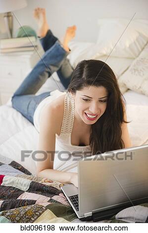 Stock Photo - Mixed race woman laying on bed using laptop. Fotosearch