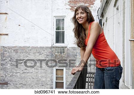 Stock Image - Mixed race woman leaning on fire escape railing. Fotosearch