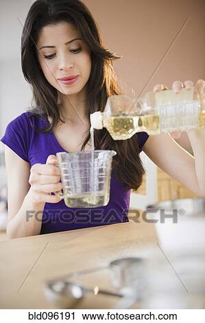 Stock Image - Mixed race woman measuring cooking oil. Fotosearch