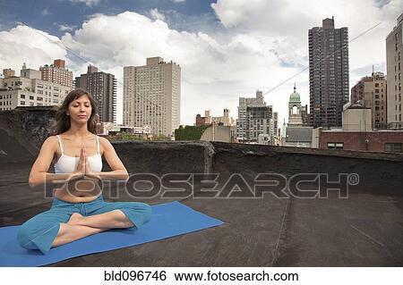 Stock Photograph - Mixed race woman practicing yoga on rooftop. Fotosearch