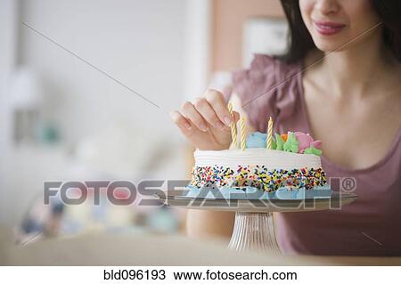 Stock Image - Mixed race woman preparing birthday cake. Fotosearch