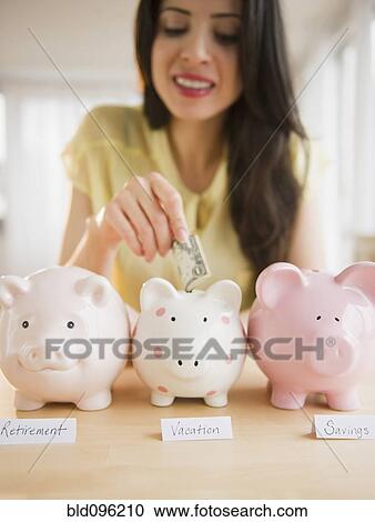 Stock Image - Mixed race woman putting money into piggy bank. Fotosearch