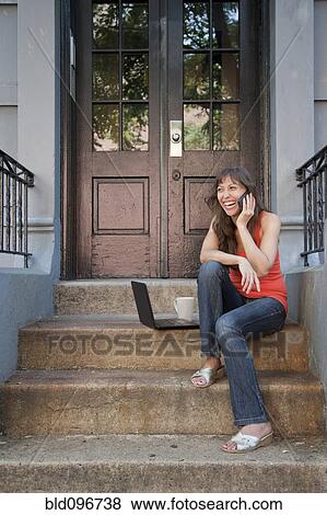 Mixed race woman sitting on front stoop with cell phone and laptop View Large Photo Image Stock Photo - Mixed race woman sitting on front stoop with cell phone and laptop. Fotosearch