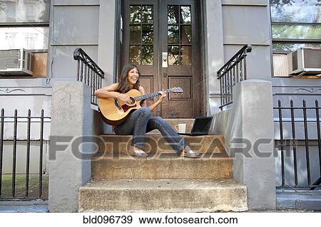 Mixed race woman sitting on front stoop playing guitar View Large Photo Image Stock Photo - Mixed race woman sitting on front stoop playing guitar. Fotosearch