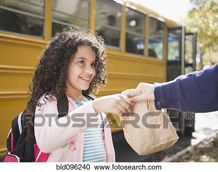 Stock Image - Mother handing daughter sack lunch. Fotosearch