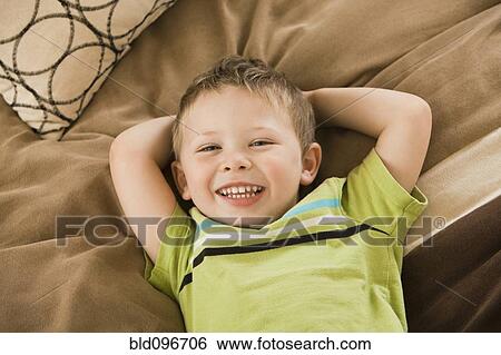 Stock Photograph - Smiling Caucasian boy laying on bed. Fotosearch