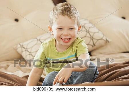 Stock Photography - Smiling Caucasian boy sitting on bed. Fotosearch