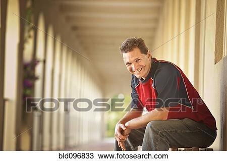 Stock Image - Smiling Caucasian man sitting outdoors. Fotosearch
