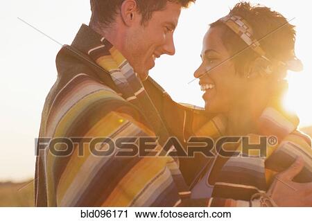 Stock Image - Smiling couple wrapped in blanket. Fotosearch