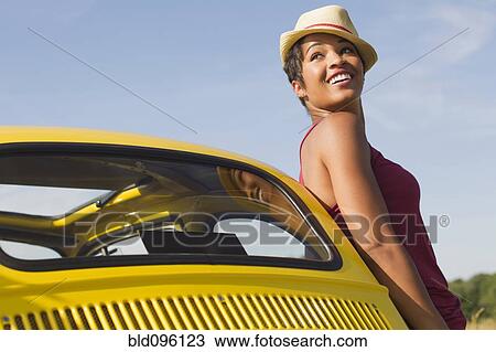 Stock Image - Smiling mixed race woman leaning on car. Fotosearch