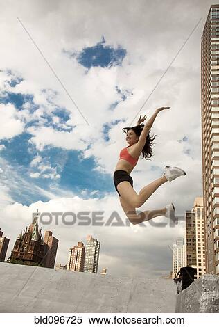 Stock Photography - Woman in sportswear jumping on roof. Fotosearch