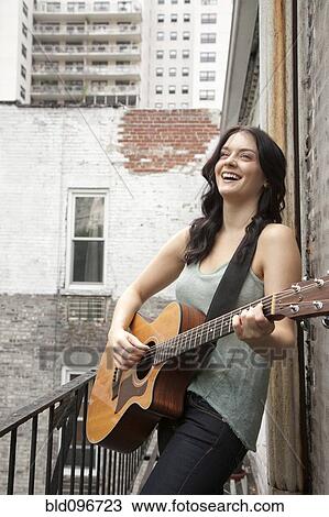 Stock Image - Woman playing guitar on fire escape. Fotosearch