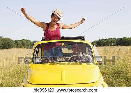 Stock Image - Woman standing in car sun roof in field. Fotosearch