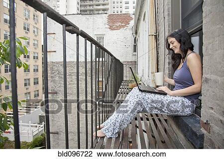 Stock Image - Woman using laptop on fire escape. Fotosearch