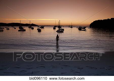 Stock Image - Young man wading in water at sunset. Fotosearch