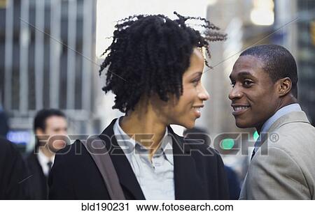 Stock Image - African American businesswoman smiling at businessman on street. Fotosearch