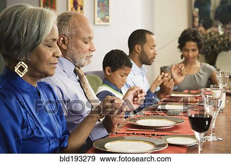 Stock Photo - African American family saying grace at dining table. Fotosearch