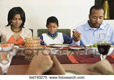 Stock Photography - African American family saying grace at dining table. Fotosearch