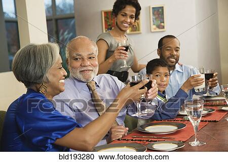 Stock Image - African American family toasting with wine at dining table. Fotosearch
