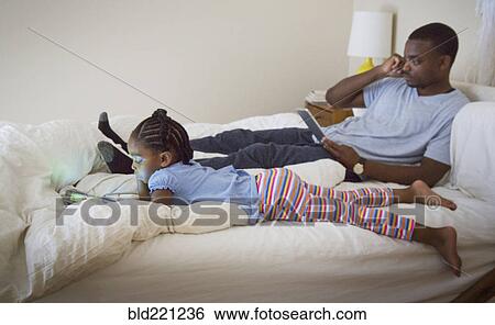 Stock Photograph - African American father and daughter relaxing on bed. Fotosearch