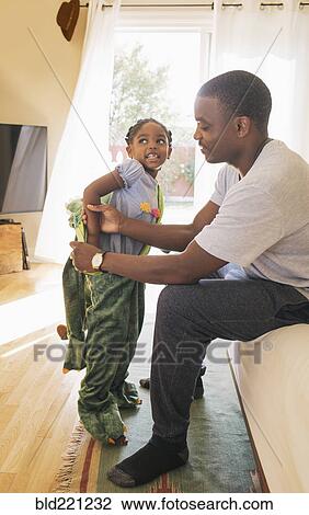 Stock Image - African American father helping daughter put on costume. Fotosearch