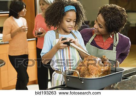 Stock Image - African American girl basting Thanksgiving turkey. Fotosearch