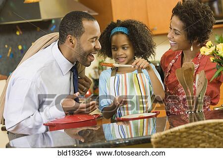 Picture - African American girl giving father a taste of sauce. Fotosearch