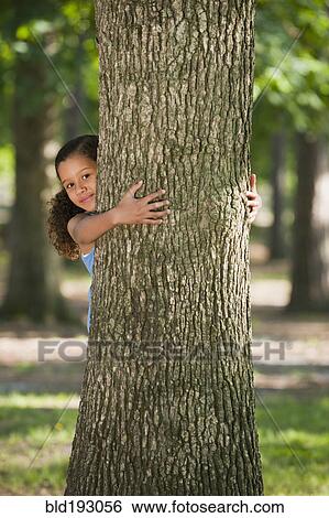Stock Photograph - African American girl hugging tree trunk. Fotosearch