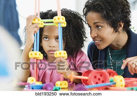 Stock Image - African American girl playing with toy while mother watches. Fotosearch