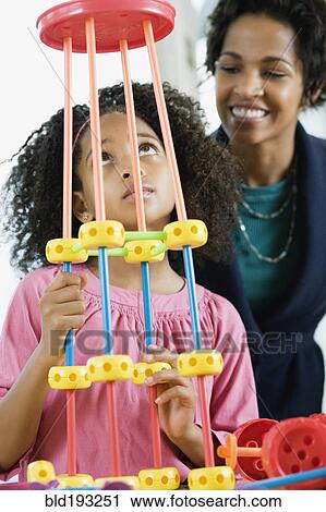 Stock Image - African American girl playing with toy while mother watches. Fotosearch
