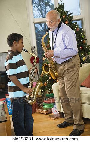 Stock Image - African American grandfather playing saxophone with grandson. Fotosearch