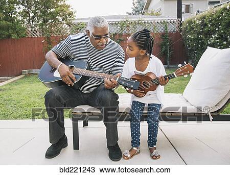 Stock Image - African American grandfather teaching granddaughter to play guitar. Fotosearch