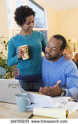 Stock Image - African American husband paying bills as wife watches. Fotosearch