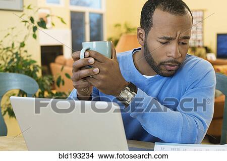 Picture - African American man drinking coffee and paying bills. Fotosearch