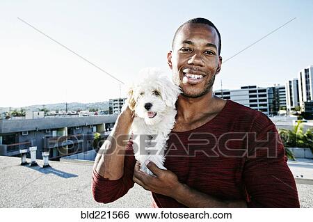 Stock Photograph - African American man holding dog on urban rooftop. Fotosearch