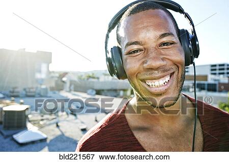 Stock Photo - African American man listening to headphones on urban rooftop. Fotosearch