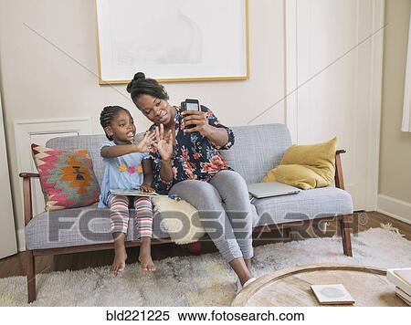 Stock Photography - African American mother and daughter taking selfie in living room. Fotosearch