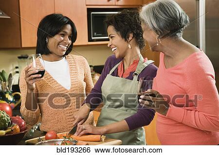 Stock Photograph - African American mother and daughters cooking and talking in kitchen. Fotosearch