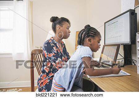 Stock Image - African American mother with daughter working from home. Fotosearch
