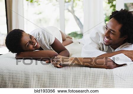 Stock Photograph - African American woman laying with boyfriend on bed. Fotosearch