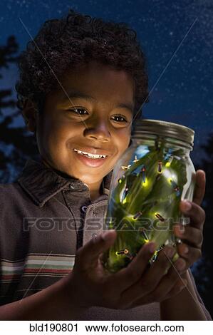 Stock Image - African boy looking at fireflies in jar. Fotosearch