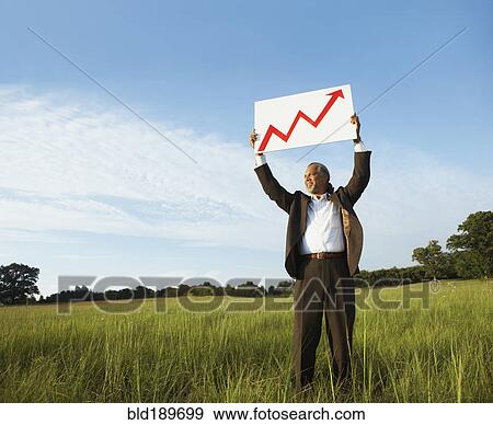 Stock Photo - African businessman holding up arrow graph in field. Fotosearch