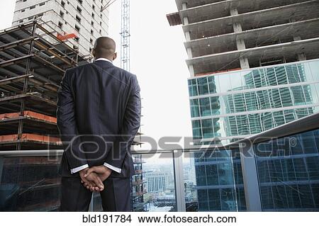 African businessman looking at skyscraper construction from balcony View Large Photo Image Picture - African businessman looking at skyscraper construction from balcony. Fotosearch