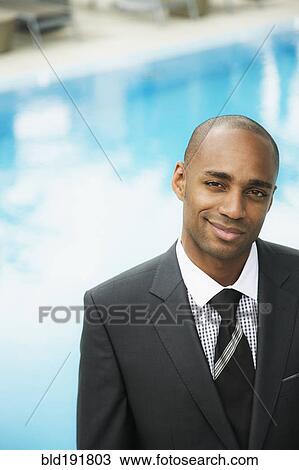 Stock Image - African businessman smiling poolside. Fotosearch